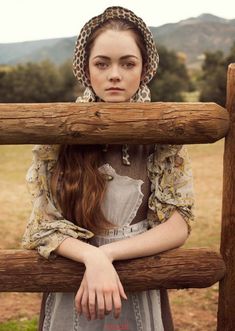 a young woman standing behind a wooden fence