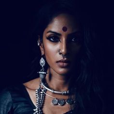 a woman with black makeup and jewelry on her face, posing for a photo in the dark