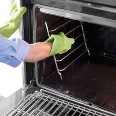 a person wearing green gloves is pulling something out of an oven