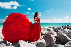 a woman in a red dress standing on rocks near the ocean