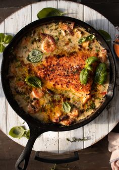 a skillet filled with food sitting on top of a wooden table next to vegetables