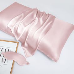 pink satin sheets and pillow on top of a white table next to a framed photograph