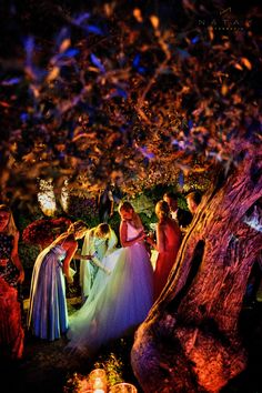 a group of people standing around each other in front of a tree with lights on it