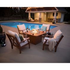 an outdoor patio with chairs and table next to a swimming pool at night, surrounded by string lights