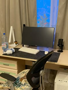 a desk with a computer, keyboard and chair in front of a curtained window