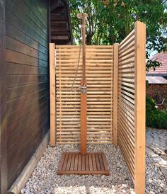 an outdoor shower with wooden slats in the background and rocks on the ground next to it