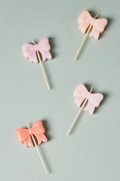 four pink bows are sitting on top of some toothpicks, one is orange and the other is pink