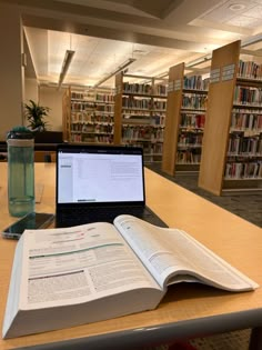 an open book sitting on top of a table next to a laptop computer and bookshelves