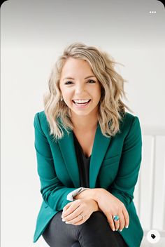 a woman sitting on top of a chair wearing a green blazer and black pants