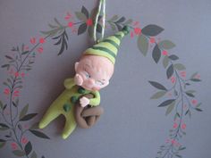 a green elf keychain hanging from a hook on a wall with flowers in the background