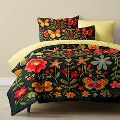 a bed covered in a black and yellow comforter next to a wall with flowers on it