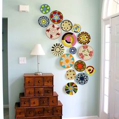 the wall is decorated with many colorful plates on it's side, along with a lamp and dresser