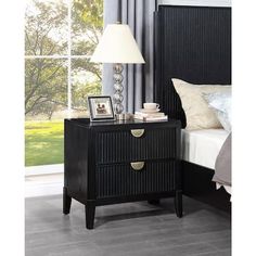 a night stand with two drawers and a lamp next to it on top of a bed