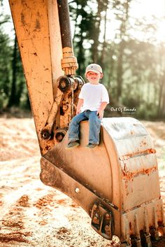 a little boy sitting on top of a bulldozer in the dirt with trees in the background