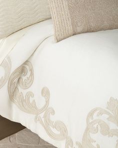 a close up of a bed with white and beige linens on top of it