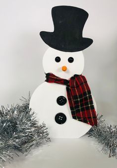 a snowman with a black hat and red plaid scarf standing in front of silver tinsel