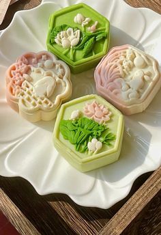 four soaps on a white plate with green leaves and flowers in the middle, sitting on a wooden table