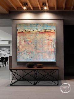 an abstract painting hangs on the wall above a table with two vases in front of it