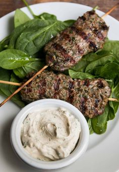 two meat patties on skewers with spinach leaves and a small bowl of ranch dressing