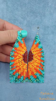 a pair of colorful beaded earrings is being held by a person's hand