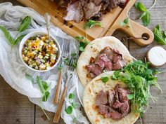 two pita breads with meat and vegetables next to a bowl of salad on a cutting board