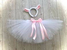 a white tutu skirt with pink bows and a bunny ears headband on a wooden floor