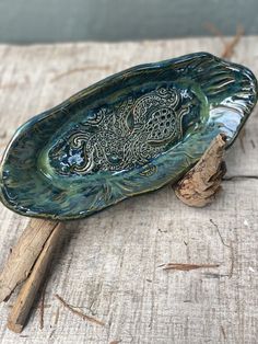 a green bowl sitting on top of a piece of wood next to a twig