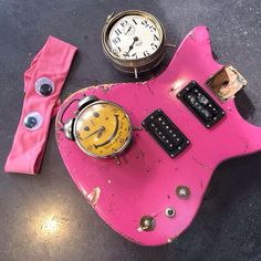 a pink guitar with a smiley face on it next to a watch and other items