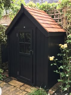 a small black shed sitting in the middle of a garden