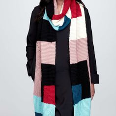 a woman wearing a multicolored knitted scarf and black top standing in front of a white background