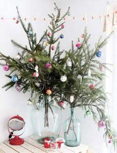 a small christmas tree in two vases on a table with ornaments hanging from it