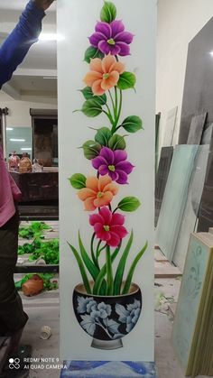 a woman is painting flowers in a vase on a wall next to other art work