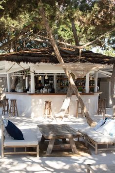 an outdoor bar with lounge chairs and tables in front of it, surrounded by trees