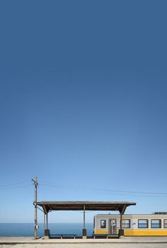 the train is parked on the side of the road next to the beach and water