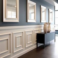 three white vases sitting on top of a black table next to two framed pictures