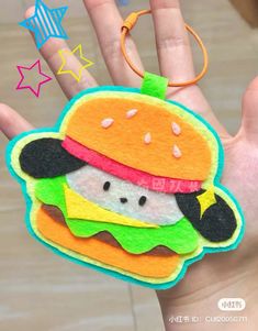 a hand holding a small felt toy with a hamburger on it's face and a star in the background