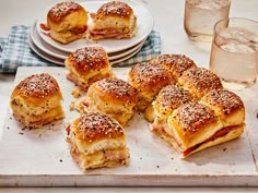 ham and cheese sliders on a cutting board next to plates with glasses of water