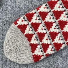 a red and white knitted sock laying on top of a gray carpet next to a pair of scissors