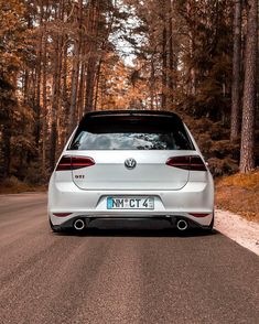 the rear end of a white car driving down a road in front of some trees