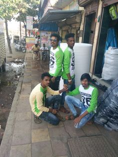 four men in green shirts sitting on the sidewalk