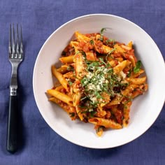 a white plate topped with pasta covered in sauce and parmesan cheese next to a fork