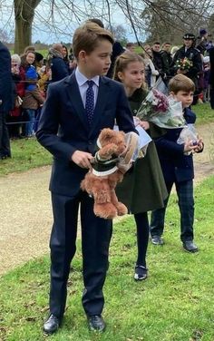 two boys in suits and ties holding teddy bears while others watch from the sidelines