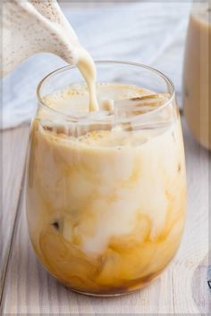 a person pouring milk into a glass filled with ice cream on top of a wooden table