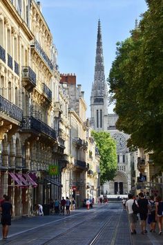 people are walking down the street in front of some buildings and a church steeple