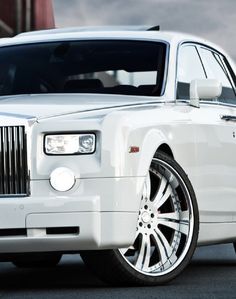 the front end of a white rolls royce parked in a parking lot next to a building