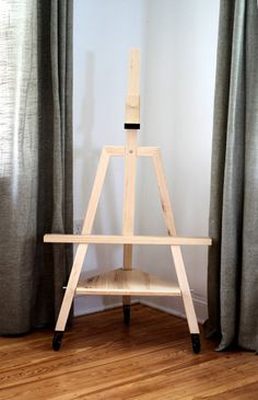 a wooden easel sitting on top of a hard wood floor next to a window