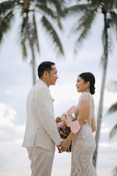 a man and woman standing next to each other near palm trees