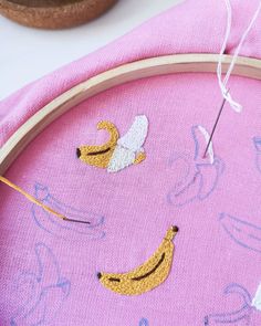 an embroidery project with bananas and angel wings on it, next to a wooden hoop