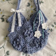 a blue crocheted purse with white flowers on the front and side hanging from it