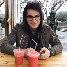 a man sitting at a table with two drinks in front of him and looking at his cell phone